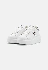 Vita plattformssneakers med slätt syntetiskt övermaterial, snörningsdesign, rund tå och svart detalj vid hälen. Har en logotypdetalj på sidan.