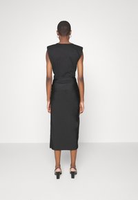 Schwarzes ärmelloses Kleid mit Schulterpolstern, tailliertem Oberteil und bodenlangem Rock. Mit Raffungselementen und glatter Textur.