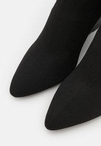 Bottines noires à bout pointu en tissu texturé avec un motif en maille. Elles présentent une finition lisse et une forme élégante.