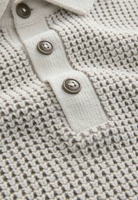 Polo din tricot bej și crem, cu un model texturat, trei butoane maro și un guler pentru un aspect structurat.