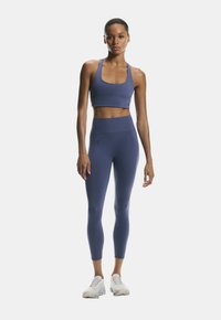 Top corto atlético de color azul marino y leggings de tejido elástico, con un diseño ajustado y elementos de marca mínimos, combinados con zapatillas blancas.