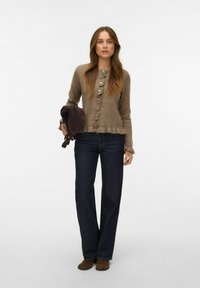 Brūns adīts kardigans ar apaļu izgriezumu, volānu malu un dekoratīvām pogām, kombinēts ar tumši ziliem džinsiem un brūnām potīšu zābakām.