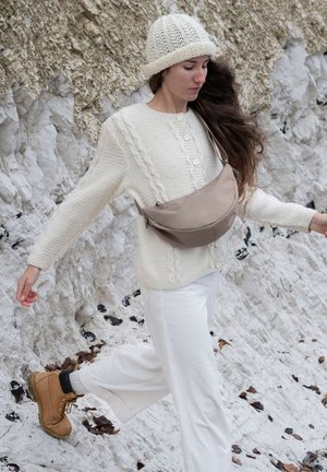 Maglione lavorato a maglia crema con motivo a trecce, abbinato a pantaloni in corduroy avorio e stivali marroni. Borsa a tracolla beige e berretto di maglia bianco.