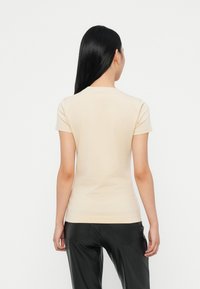 Camiseta ajustada beige de manga corta, de textura suave, con cuello redondo y un diseño sencillo, combinada con pantalones negros.