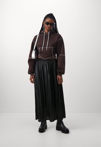 Brun kort hoodie med vit sömnad, i kombination med en svart veckad kjol och svarta klumpiga stövlar. Accessoarer med små svarta solglasögon.