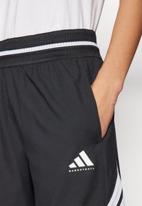 Melni sporta šorti ar elastīgu jostasvietu, sānu kabatām un baltām svītrām. Satur baltu Adidas logotipu ar tekstu "BASKETBALL".
