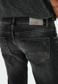 Jean en denim gris foncé avec une finition texturée, poches standard et une étiquette en cuir avec la marque "Only & Sons" au dos.