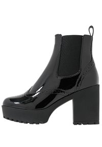 Botas de tobillo de charol negro con un tacón alto y grueso, paneles laterales elásticos y una suela de goma texturizada con un patrón de tacos.