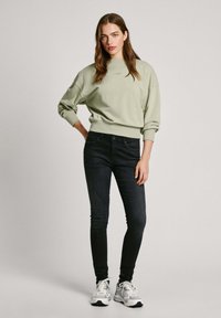 Šviesiai žalias megztinis su apvaliu kaklu ir plačiu kirpimu, derinamas su tamsiomis liesomis džinsais ir baltais sportbačiais. Atsitiktinis, patogus apranga.