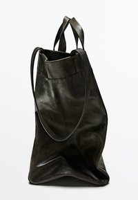 Svart läder tote-väska med texturerad yta, utrustad med dubbla handtag och en rymlig öppning. Mjuk, ostrukturerad form med en plan botten.