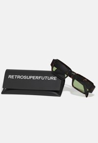 Occhiali da sole tartaruga marrone con lenti verdi, design della montatura quadrata e logo stampato su un astuccio protettivo nero.