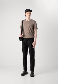 Brun kortermet t-skjorte med logo, svarte drawstring-bukser, svarte sko og en svart caps. Enkel design, uformell antrekk.