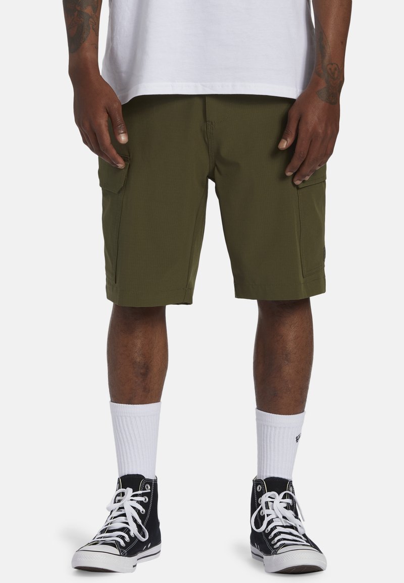 Shorts cargo vert olive avec deux poches latérales, coupe droite et ourlet cousu, associés à des chaussettes blanches et des baskets montantes noires.