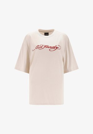 Beige ylin painettu T-paita, jossa on punainen kaareva "Ed Hardy" -logo rinnan kohdalla ja pyöreä pääntie.