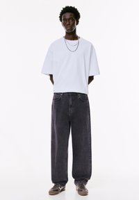 Weißes, übergroßes T-Shirt, dunkelgraue, sackartige Jeans und Sneakers. Ausgestattet mit geschichteten Silberketten und strukturiertem, ungebändigtem Haar.