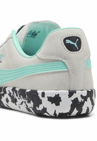 Puma-sneakers med en lysegrå ruskindsoverdel, mintgrøn stribe og sorte logo detaljer. Strukturert sort-hvid mønstret sål tilføjer detalje.