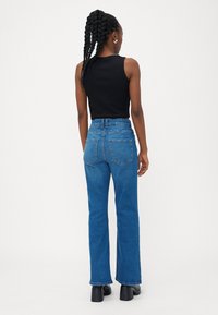 Tamne visoki plavi traperice s ravnim krojem, s stražnjim džepovima i vidljivom šavom. Uparene s crnom majicom na bretele.