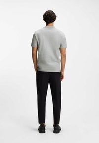 Jasnoszara koszula z krótkim rękawem, okrągłym dekoltem, w połączeniu z czarnymi spodniami o gładkim kroju oraz czarnymi trampkami. Proste, czyste linie.