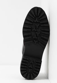 Semelle de chaussure en caoutchouc noir avec motif de crampons texturés comprenant des rainures et des stries, indiquée en taille 37. Design simple et fonctionnel.