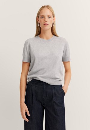 Helles graues, gestricktes Kurzarmoberteil mit rundem Ausschnitt, kombiniert mit dunklen Jeanshosen mit bequemer Passform und Vorderfalten.