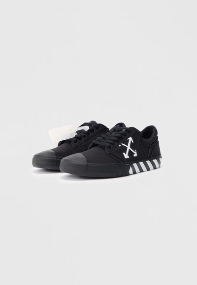 Sneaker in tela nera con punta in gomma, logo bianco e suola a righe bianche e nere. Presenta un design con lacci e un'etichetta laterale.