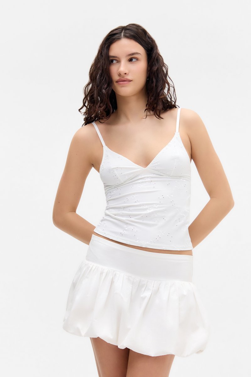 Valkoinen camisole, jossa on ohuet olkaimet ja kukkakirjontaa, yhdistettynä valkoisiin, liehuviin hameeseen, joka on valmistettu sileästä kankaasta ja jossa on joustava vyötärö.