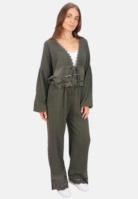 Olivgrünes Zweiteiler-Outfit aus strukturiertem Stoff; mit Spitzenbesatz und einer Schleife an der Vorderseite des Tops, dazu lockere, weite Hose.