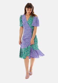 Wrap dress featuring a mix of purple and green patterns, short puff sleeves, a flared hem, and lightweight fabric.