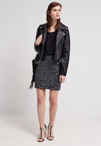 Veste de motard en cuir noir portée sur un haut noir, associée à une jupe texturée à sequins noirs et blancs. La tenue est complétée par des talons aiguilles à brides.