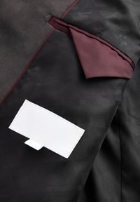 Tessuto nero con motivi geometrici, caratterizzato da un dettaglio della tasca color marrone e un'etichetta bianca con linguetta. Superficie texture con colori a contrasto.