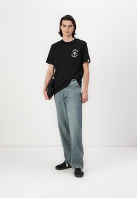 Svart bomulls t-skjorte med et sirkulært grafisk motiv på brystet, kombinert med lyseblå rette jeans og svarte sko.