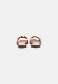 Braune flache Sandalen mit goldenen Akzenten, offenen Zehen und minimalistischen Design. Die Sohle hat eine dunkle Holzoptik mit einer glatten Innenfläche.