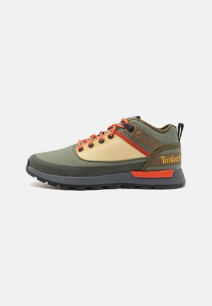 Chaussure de randonnée Timberland verte, beige et orange avec lacets orange, semelle noire et languette sur fond blanc.