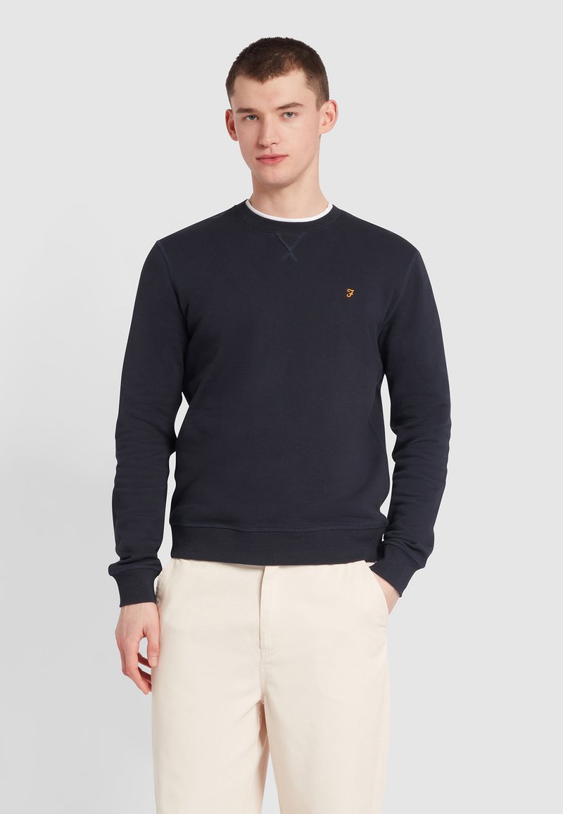 Granatowa bluza crewneck wykonana z bawełny, z prążkowanymi mankietami i dolnym wykończeniem, z małym żółtym logo na piersi i klasycznym krojem.