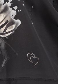 Zwarte stof met een bedrukt rozenpatroon in grijstinten en een accent van een rhinestone hart. Gladde textuur met een subtiele glans.