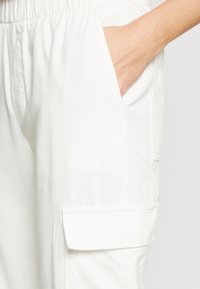 Witte katoenen cargobroek met een elastische tailleband, zijzakken en een klepzak op de dij. Glad textuur en casual ontwerp.