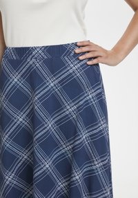 Laivastonsininen hame, jossa on valkoinen ruudullinen kuosi, joustava vyötärö ja pehmeä kangas. Lähikuva näyttää käden lepäävän vyötärön kohdalla.