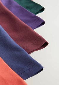 T-shirts en coton de différentes couleurs : vert, violet, bordeaux, marine et corail, présentés avec des manches retroussées et une texture côtelée.