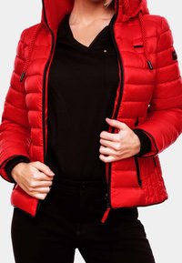 Röd vadderad jacka med huva, med dragkedjestängning, quiltat mönster och svarta detaljer vid ärmar och nederkant, bärs över en svart topp.