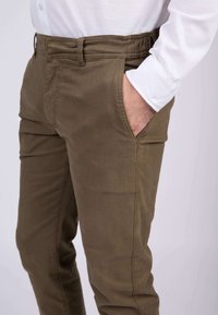 Pantalons en mélange de coton vert olive avec une taille élastique, poches latérales et une texture lisse. Présente des détails de couture le long des coutures.