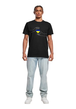 Schwarzes Baumwoll-T-Shirt mit einem weißen Linienz drawing von zwei Händen, die ein Herz halten, mit blauem und gelbem Farbzentrum. Lässiger Schnitt.