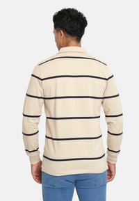 Polo de manga larga beige con rayas horizontales en marino. Tela suave, corte relajado y cuello tipo solapa. La vista trasera muestra las costuras de los hombros.