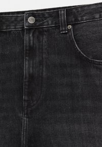 Gros plan sur un jean en denim noir montrant le bouton, la boucle de ceinture, la poche avant et les détails de couture.