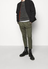 Svart bomberjacka med orange dragkedja, grå sweatshirt med rund hals, olivgröna tapered byxor och svarta snörstövlar. Släta texturer.