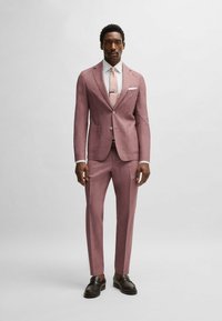 Rosa skräddarsydd kostym med en strukturerad finish, vit skjorta och matchande slips. Bruna loafers fulländar outfiten.