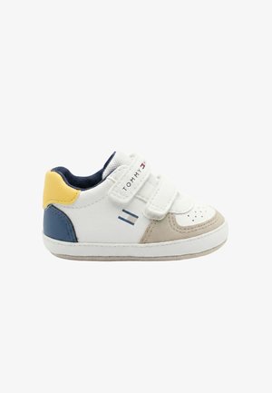 Scarpa da ginnastica bianca per bambino piccolo con cinturini in Velcro, punta beige, accenti blu e gialli sul tallone e logo Tommy Hilfiger sul lato e sul cinturino.