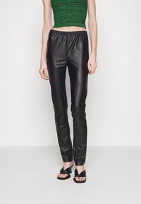 Černé kožené kalhoty s elegantním, zúženým střihem a elastickým pasem, doplněné o zelený pletený crop top a černé sandály.