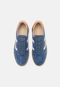 Blaue Wildleder-Sneaker mit weißen Streifen, braunen Sohlen und orangefarbenen Akzenten an den Fersen. Mit runder Zehenpartie und flachen Schnürsenkeln.