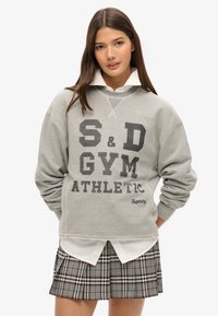 Grå sweatshirts med "S&D GYM ATHLETIC" grafik i sort, struktureret stof og ribbede manchetter, lagt over en hvid skjorte med krave og en ternet nederdel.