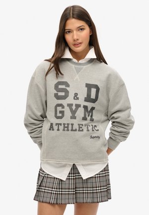 Szary sweatshirt z grafiką "S&D GYM ATHLETIC" w czerni, wykonany z teksturowanej tkaniny, z prążkowanymi mankietami, założony na białą koszulę z kołnierzykiem i spódnicę w kratkę.